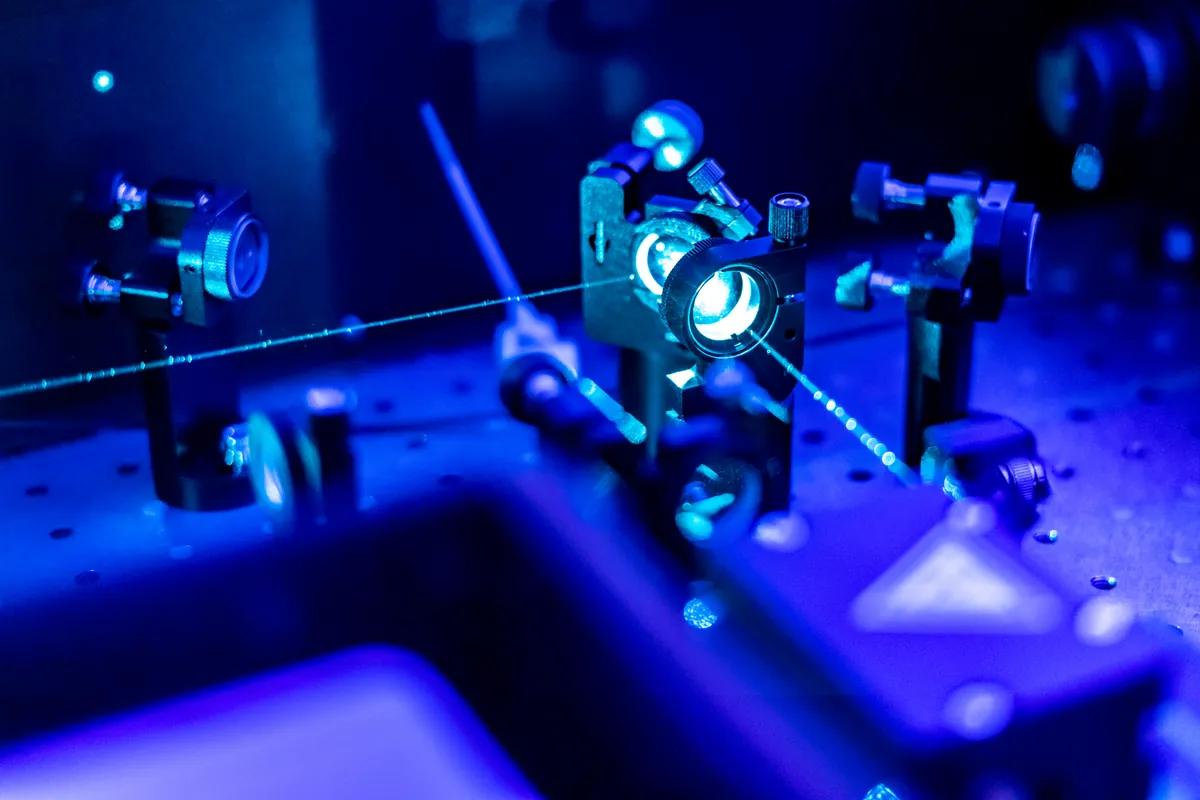 A blue laser beam crossing an optical bench through mounted lenses and mirror mounts